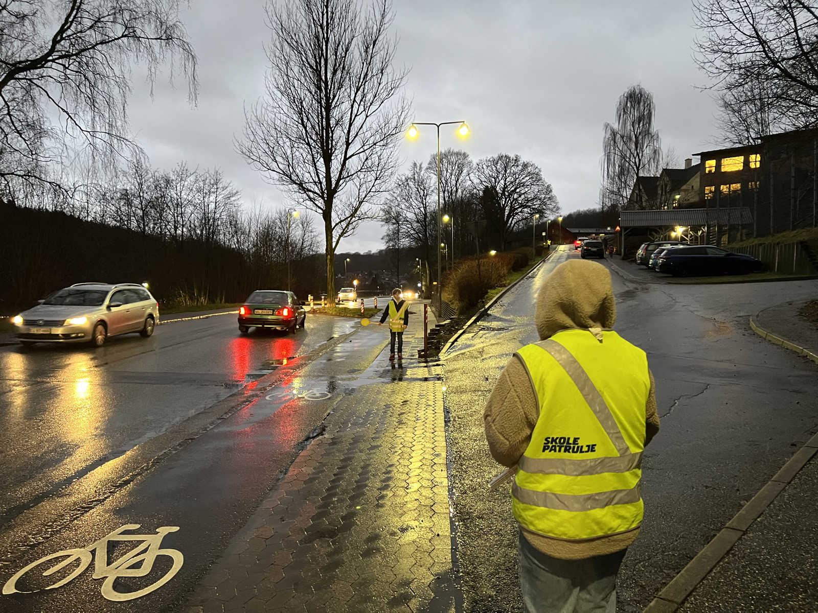 To børn står i skolepatrulje, mens biler kører forbi